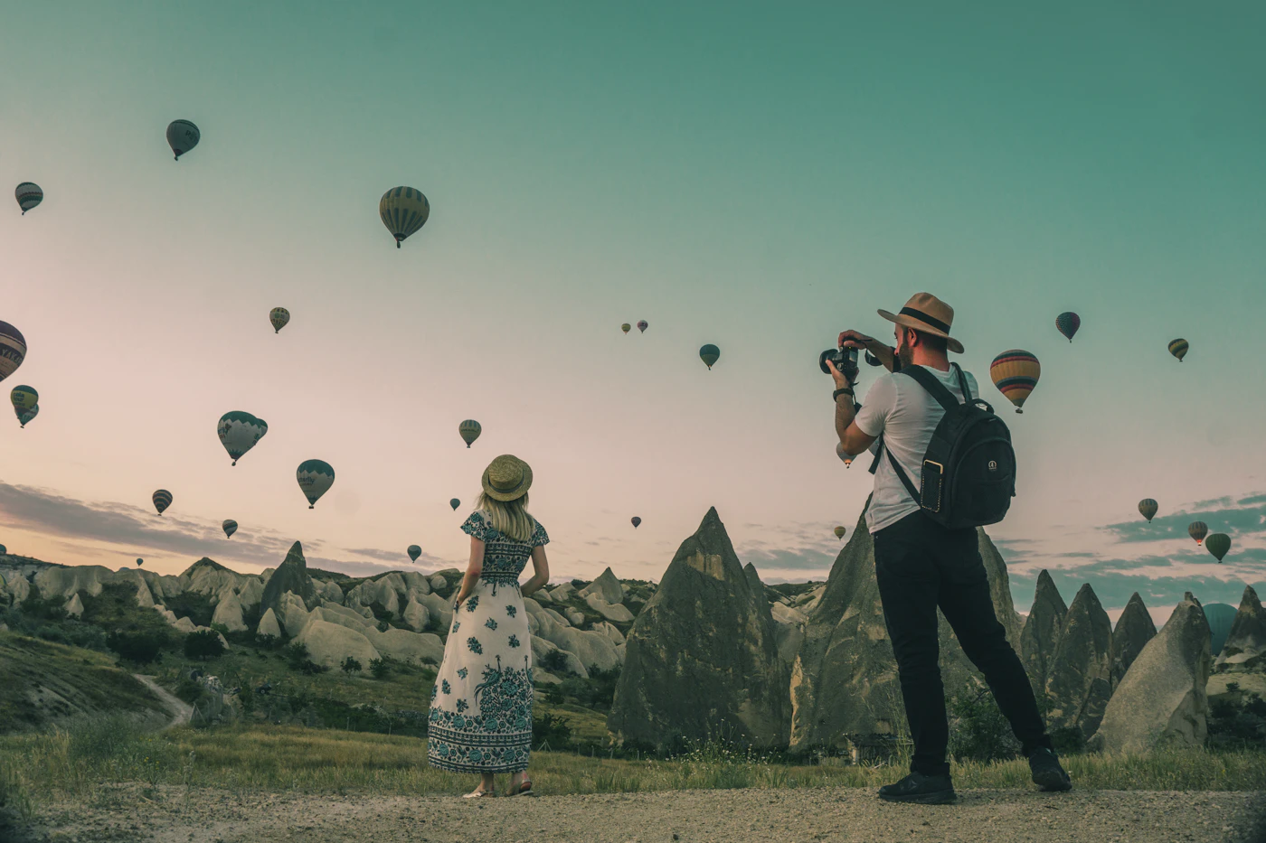 Two travelers photographing hot air balloons over Cappadocia