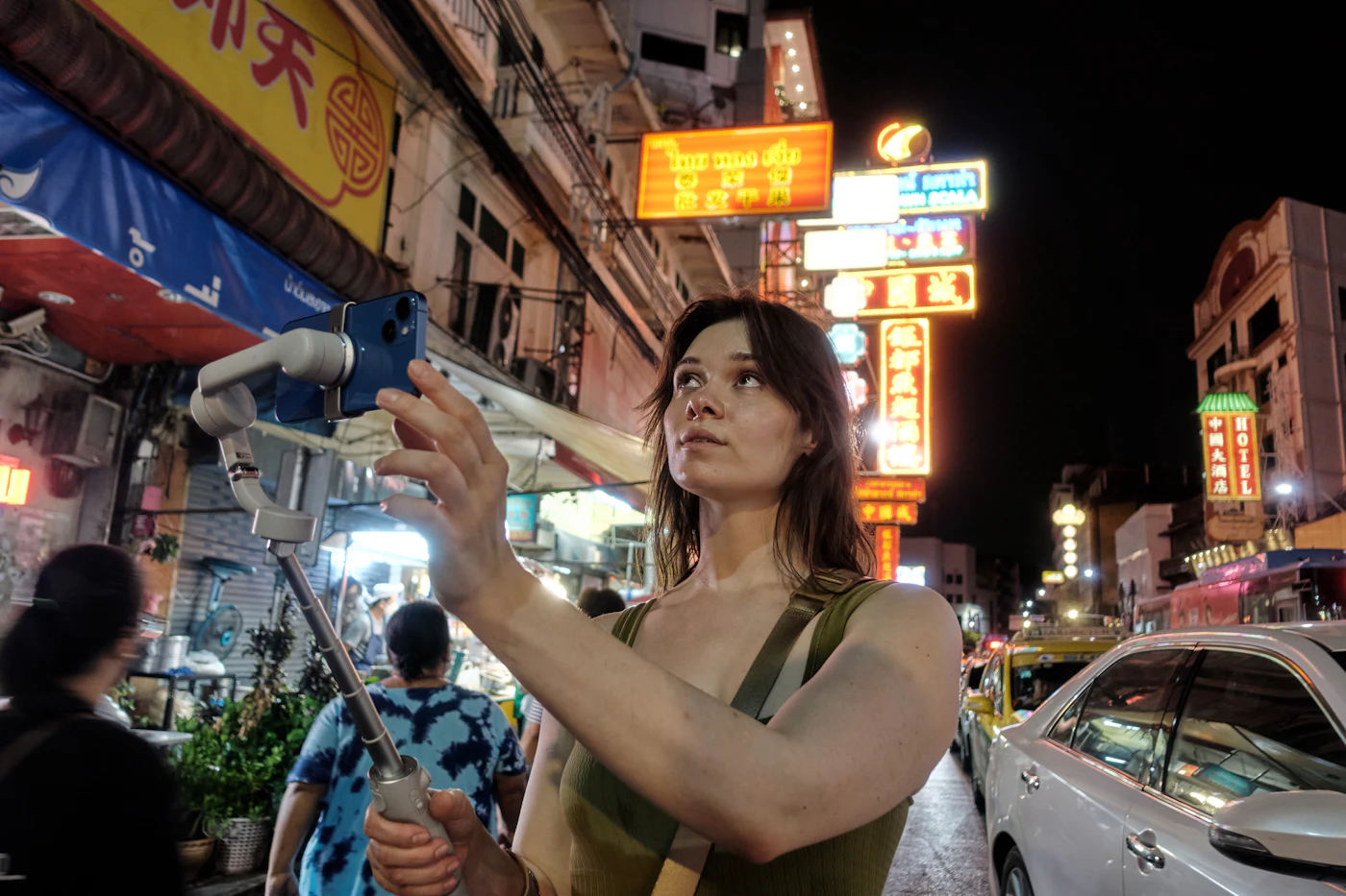 A woman filming herself with a selfie stick on a neon street at night