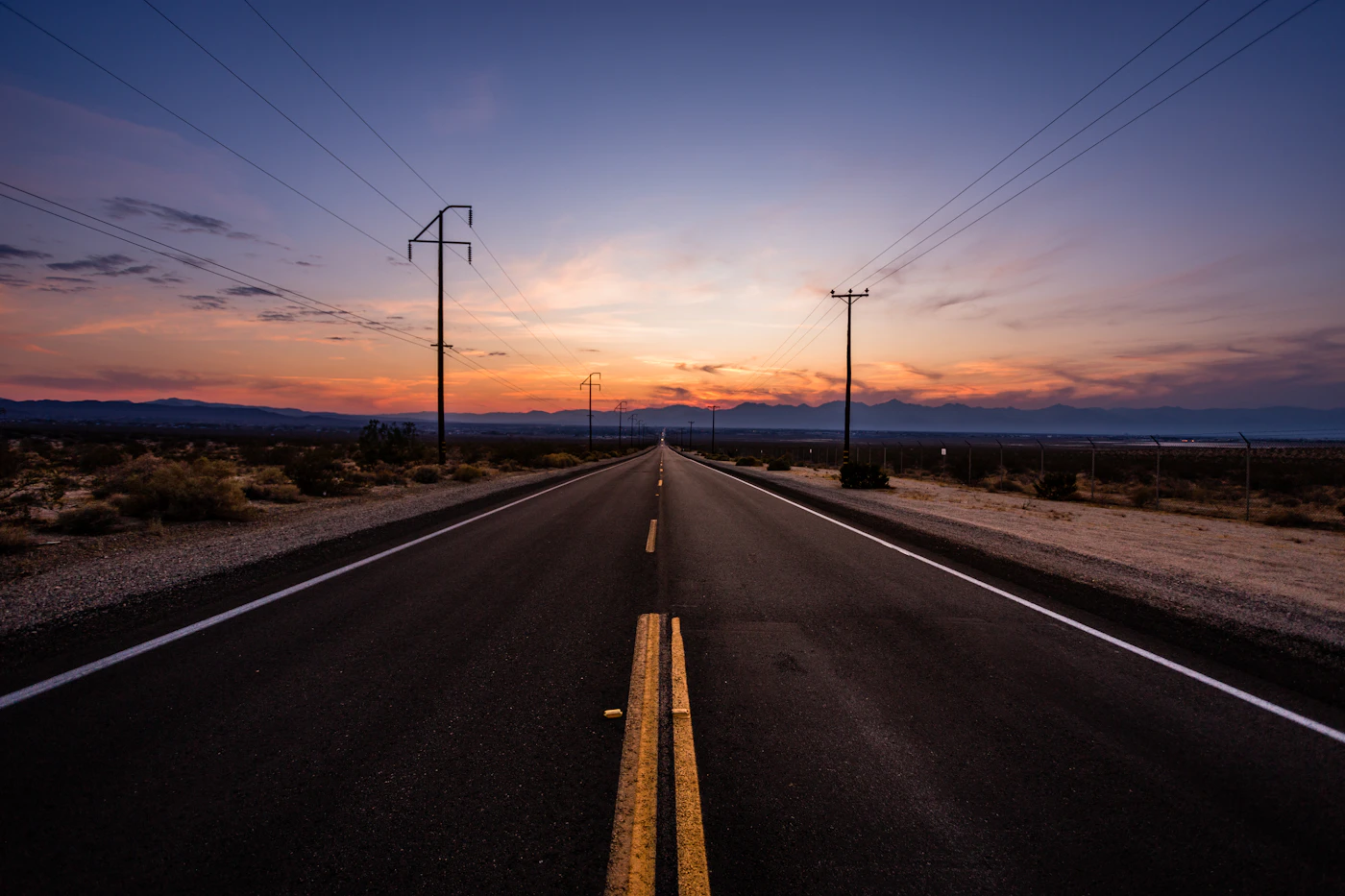 An empty highway running straight into a blazing sunset